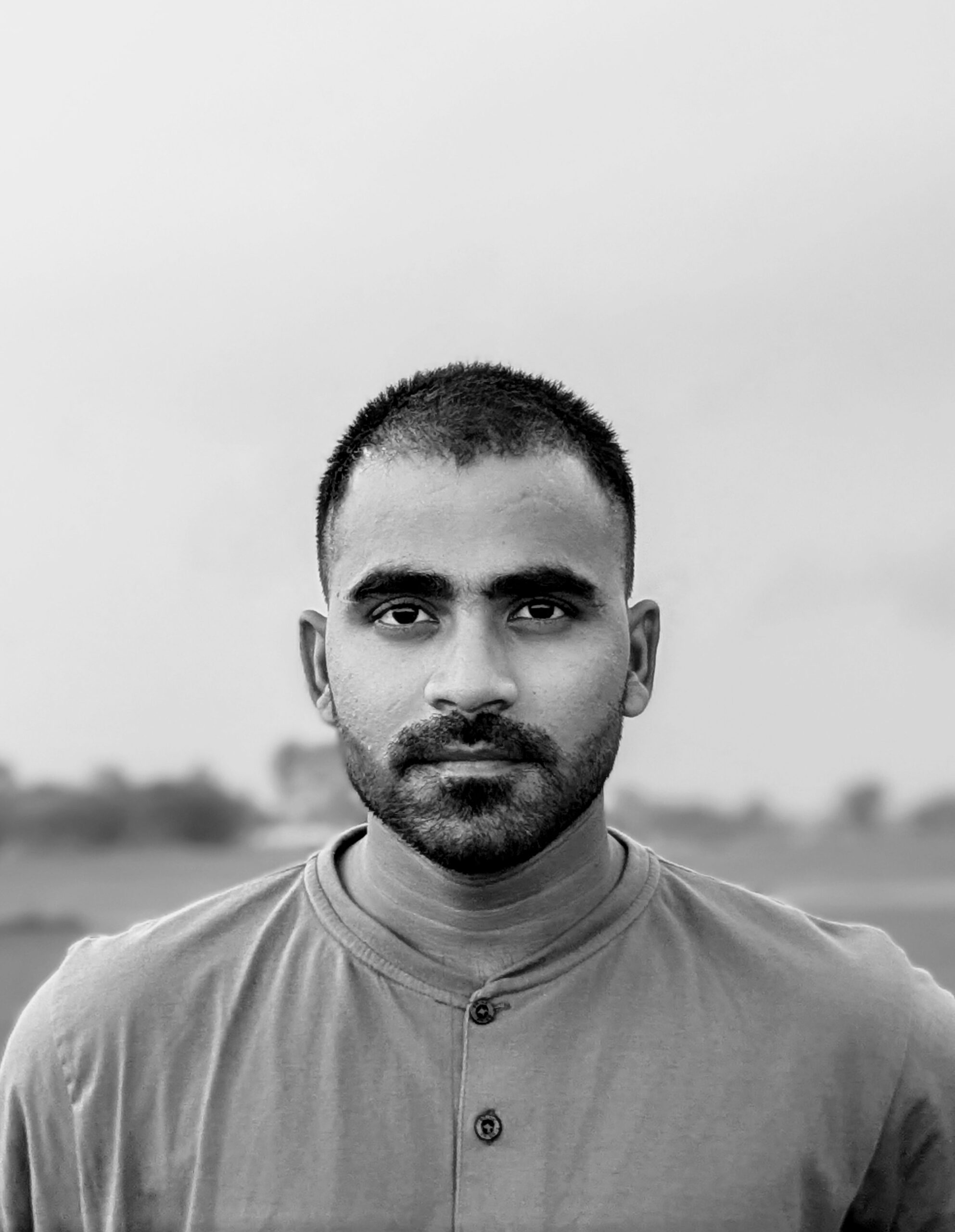 Captivating black and white portrait of a young man standing outdoors with a serious expression.